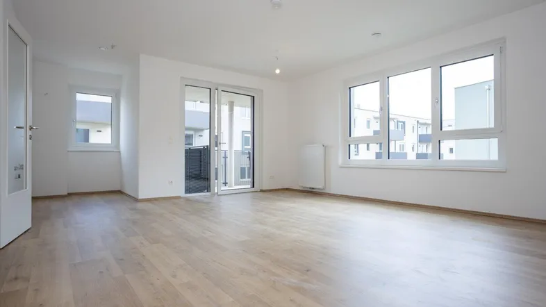 Helles Wohnzimmer mit modernem Laminatboden, großen Fenstern und Zugang zum Balkon.