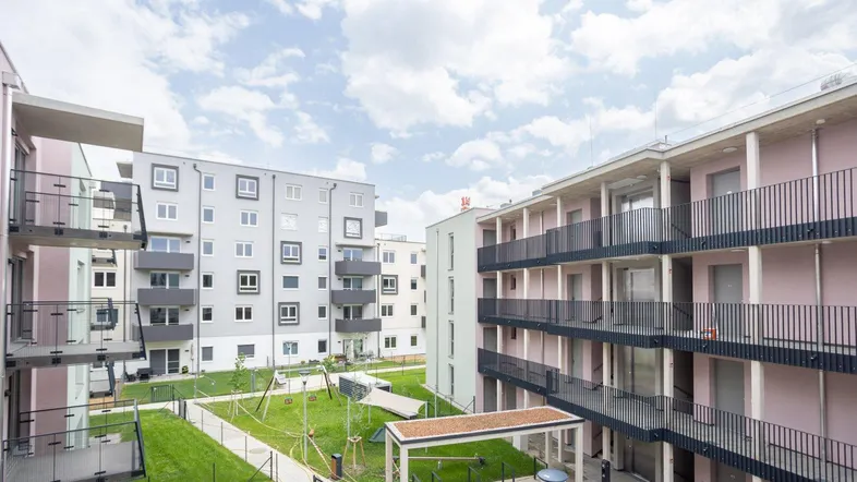 Moderner Wohnkomplex mit mehreren Gebäuden, einem zentralen Innenhof und einem Kinderspielplatz.