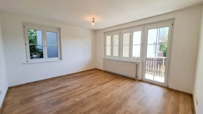 Helles Zimmer mit Laminatboden, weißen Wänden und Zugang zu einem Balkon.