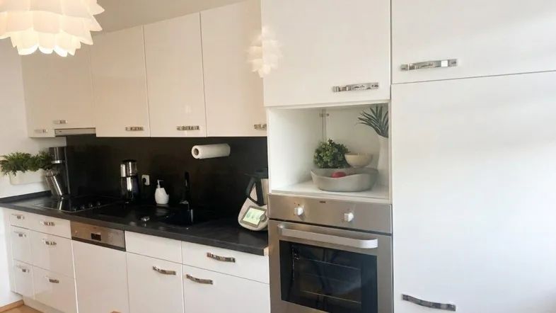 Moderne weiße Küche mit schwarzen Arbeitsplatten, integriertem Backofen und Hängeschränken.