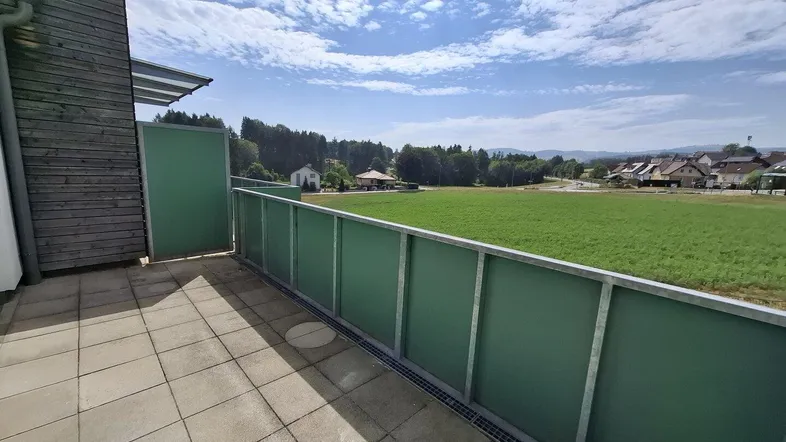 Geräumiger Balkon mit Fliesenboden und weitem Blick über grüne Felder und die Landschaft.