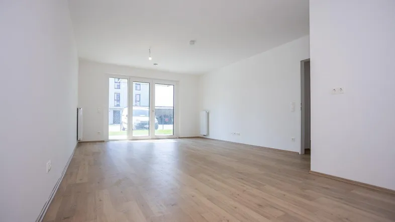 Helles, leeres Wohnzimmer mit Laminatboden und Zugang zur Terrasse in einem Neubau.