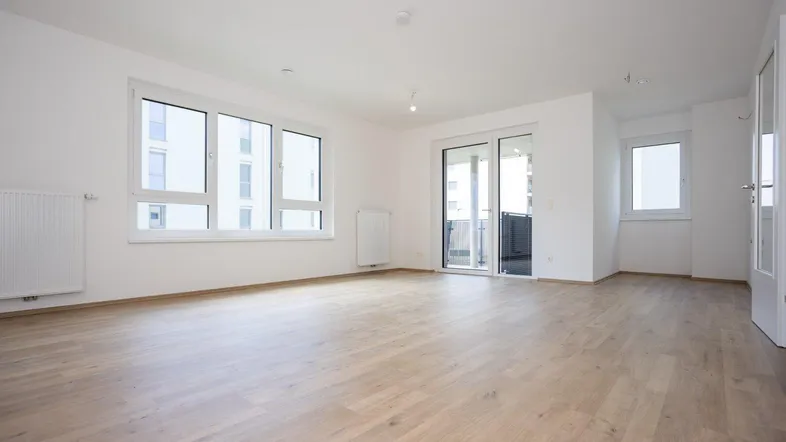 Helles und geräumiges Wohnzimmer mit großen Fenstern, Laminatboden und Zugang zum Balkon.