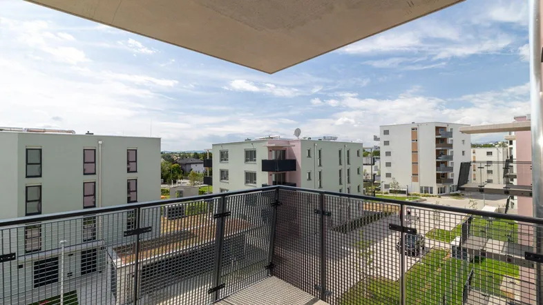 Blick von einem modernen Balkon mit Metallgeländer auf umliegende Wohngebäude und den Himmel.