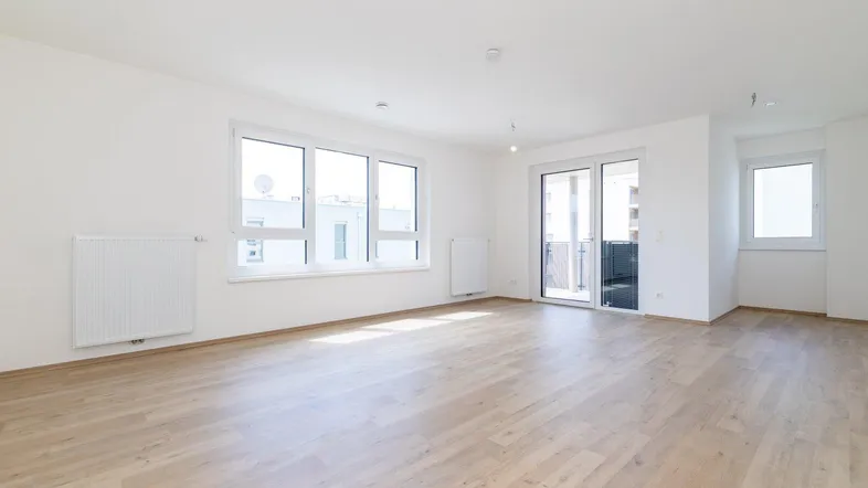 Helles, leeres Wohnzimmer mit modernem Laminatboden und Zugang zum Balkon.