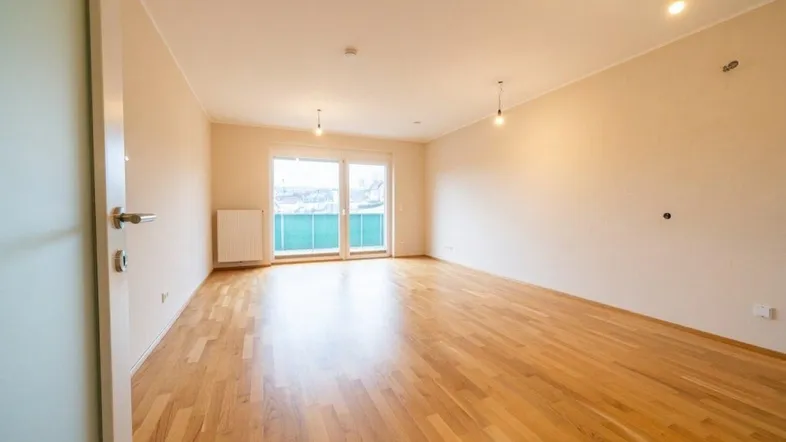 Heller, leerer Raum mit schönem Holzboden, großen Fenstern und direktem Zugang zu einem Balkon.