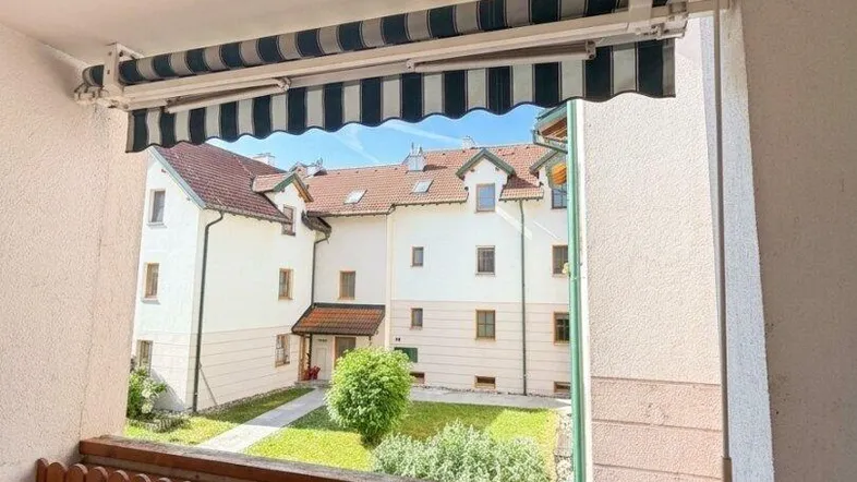 Balkon mit Markise und Blick auf den grünen Innenhof und umliegende Gebäude.