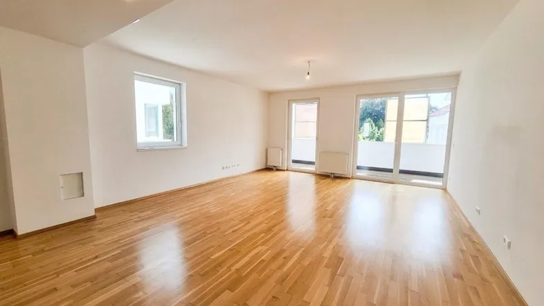Helles, leeres Zimmer mit Parkettboden und Zugang zu einem Balkon, bereit zur Gestaltung.