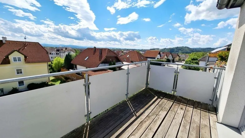 Geräumiger Balkon mit Holzboden und weitem Blick über die umliegende Landschaft und Häuser.