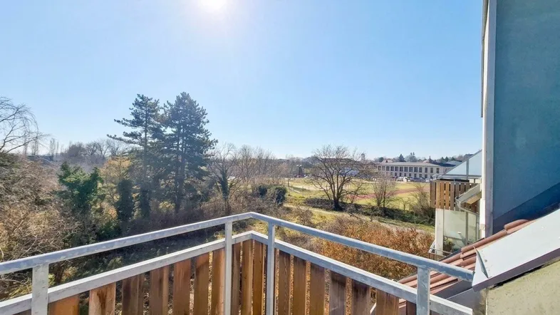 Heller Balkon mit Holzgeländer und weitem Blick ins Grüne an einem sonnigen Tag.