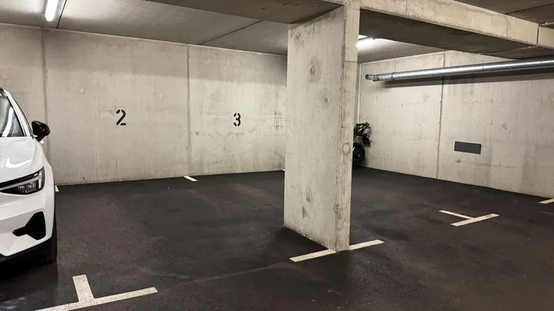 Geräumiger Tiefgaragenstellplatz mit Betonwänden, sichtbaren Rohren und heller Deckenbeleuchtung.