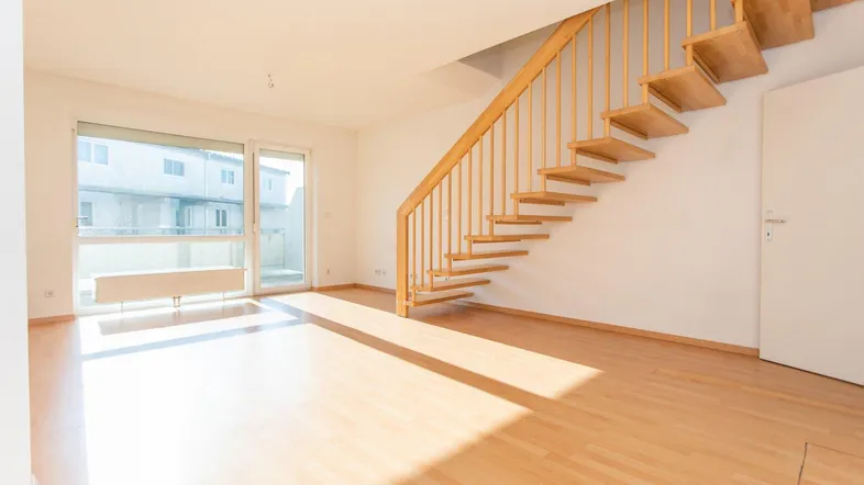 Helles Wohnzimmer mit offener Holztreppe, Laminatboden und Zugang zu einem Balkon.