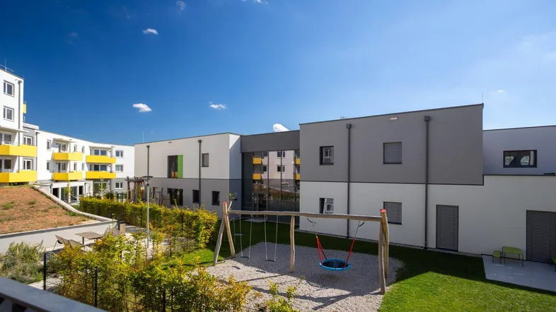 Moderner Wohnkomplex mit Spielplatz und Grünflächen, umgeben von neuen Gebäuden unter blauem Himmel.