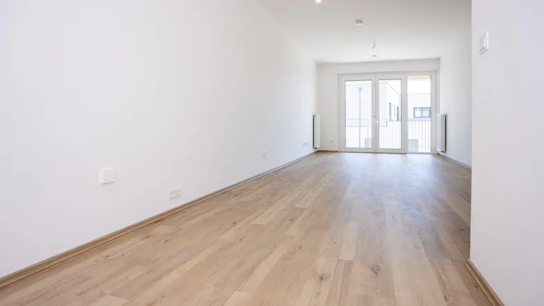 Helles, leeres Zimmer mit Holzboden und Zugang zu einem französischen Balkon.