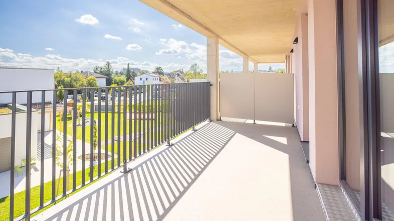 Heller Balkon mit Metallgeländer und Blick auf die grüne Umgebung unter blauem Himmel.