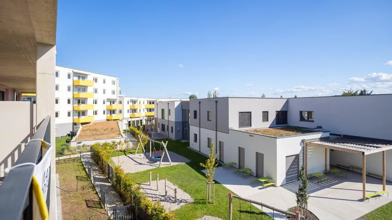 Weitläufiger Gemeinschaftsgarten mit Spielplatz und modernen Wohngebäuden unter blauem Himmel.