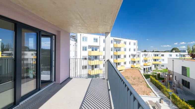 Geräumiger Balkon mit Blick auf die umliegenden Neubauten und den Innenhof unter blauem Himmel.