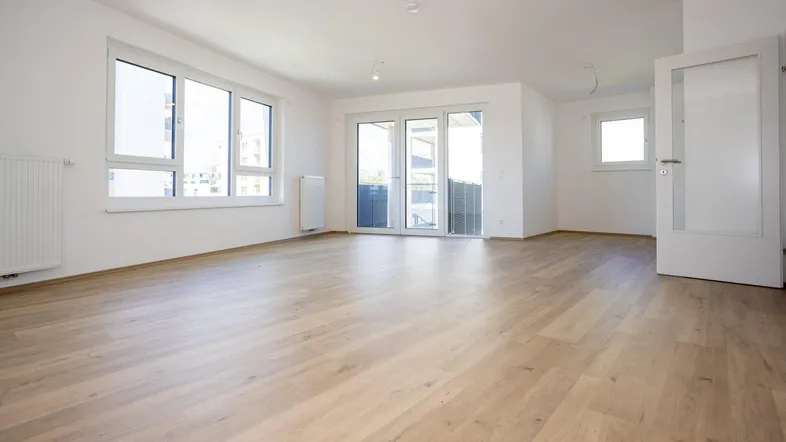 Helles und geräumiges Wohnzimmer mit großen Fenstern, Balkonzugang und modernem Laminatboden.