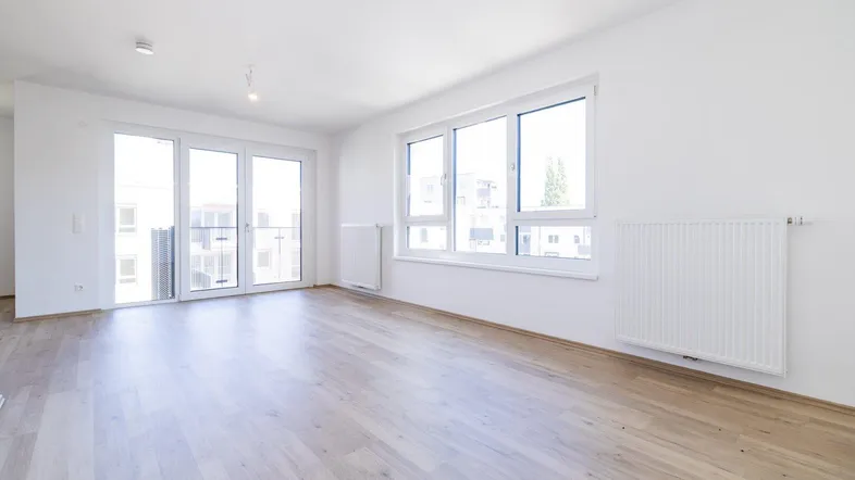 Helles, leeres Zimmer mit großen Fenstern, Balkonzugang und modernem Laminatboden.