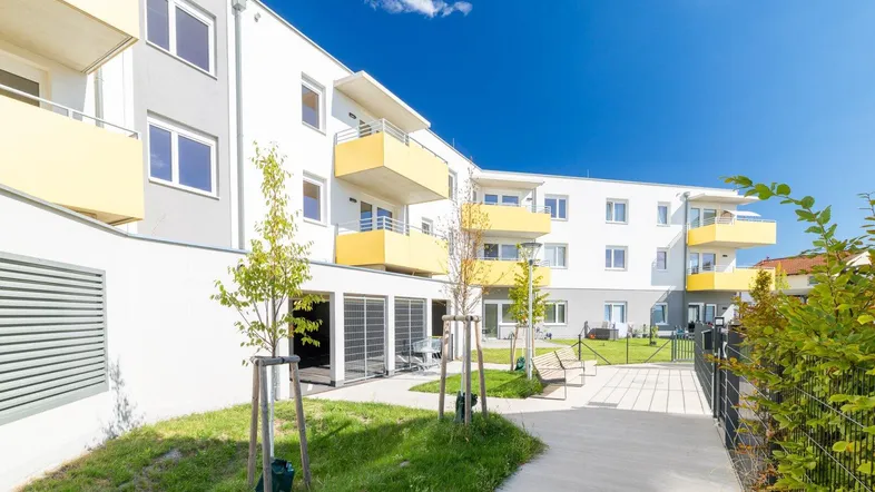 Modernes Mehrfamilienhaus mit gelben Balkonen und gepflegten Grünflächen unter blauem Himmel.