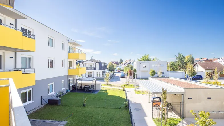 Blick von einem Balkon auf die moderne Wohnanlage mit gelben Balkonen und einer gepflegten Grünfläche.