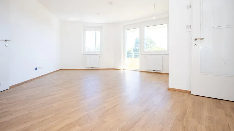 Helles, leeres Zimmer mit Laminatboden und Zugang zum Balkon, bereit für die individuelle Gestaltung.
