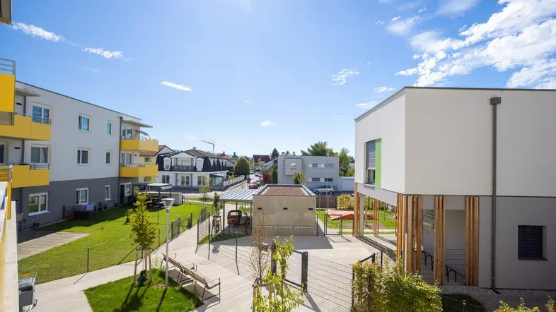 Blick auf die moderne Wohnanlage mit begrüntem Innenhof und umliegenden Gebäuden unter blauem Himmel.