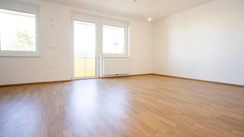 Helles, leeres Zimmer mit Laminatboden und Zugang zu einem Balkon, ideal als Wohn- oder Schlafzimmer.