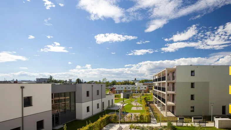 Moderne Wohnanlage mit mehreren Gebäuden, Grünflächen und einem Kinderspielplatz unter blauem Himmel.