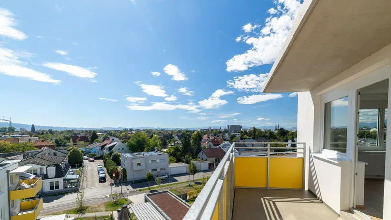 Heller Balkon mit gelbem Geländer und weitem Blick über die Stadt und die umliegende Landschaft.