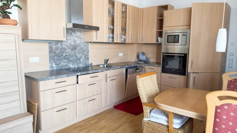 Moderne Einbauküche mit hellen Holzfronten, integrierten Geräten und einem kleinen Essbereich.