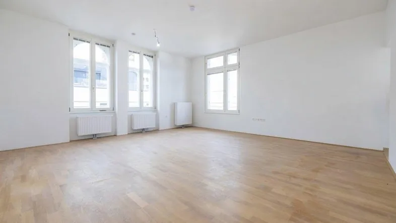Helles, leeres Zimmer mit Parkettboden und mehreren Fenstern, bereit zur individuellen Gestaltung.