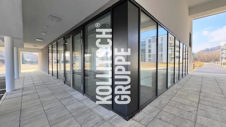 Modernes Geschäftsgebäude mit großer Glasfassade und grauem Fliesenboden im Außenbereich.