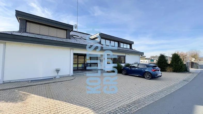 Modernes Bürogebäude mit gepflastertem Vorplatz und Parkmöglichkeiten unter blauem Himmel.