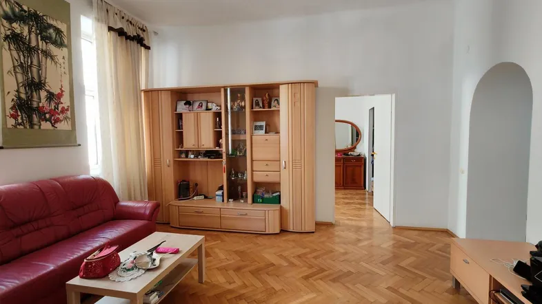 Geräumiges Wohnzimmer mit Fischgrätparkett, rotem Sofa und Holzschrankwand, hell und einladend.