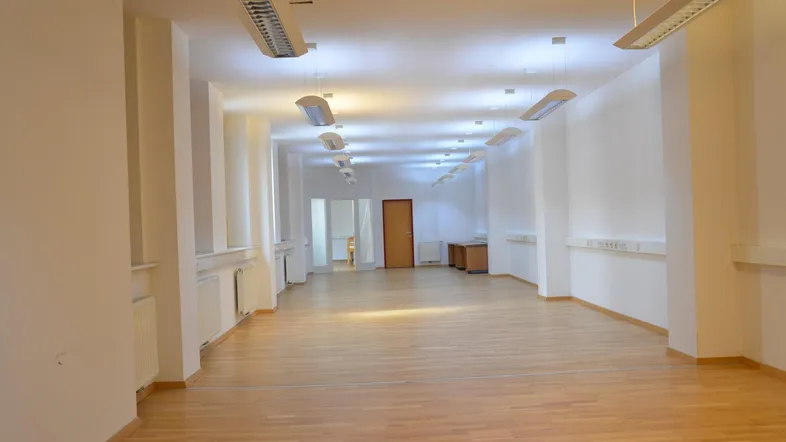 Großer, leerer Raum mit hellem Holzfußboden und Deckenleuchten, ideal für Büronutzung oder als Mehrzweckraum.