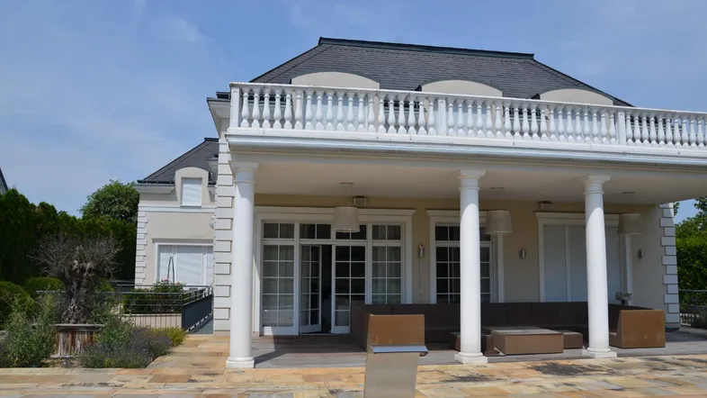 Elegante Villa mit klassischer Architektur, großer Terrasse, Säulen und Balkon.