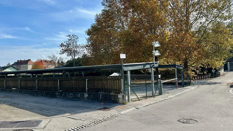 Außenansicht des Parkplatzes mit überdachten Stellplätzen und herbstlichen Bäumen im Hintergrund.