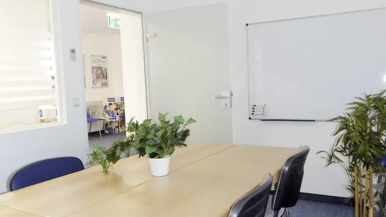 Heller Konferenzraum mit großem Holztisch, blauer Teppichboden und Whiteboard für Besprechungen.