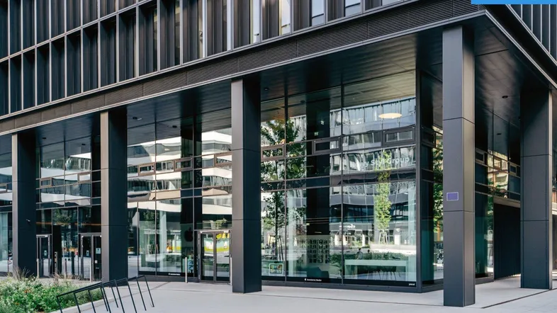 Moderner Eingangsbereich eines Bürogebäudes mit großer Glasfassade und dunklen Säulen.