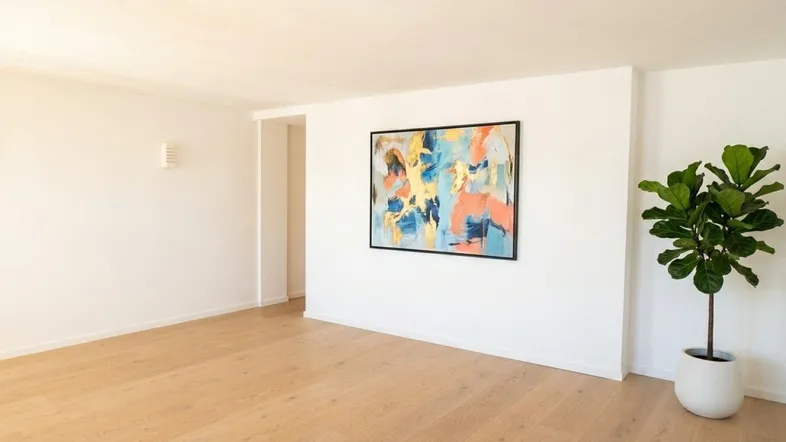 Helles, leeres Zimmer mit Holzboden und moderner Kunst an der Wand, bereit zur Einrichtung.