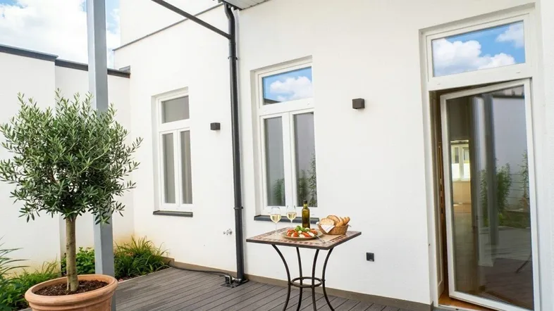 Helle Terrasse mit Holzboden, kleinem Tisch und Topfpflanze, ideal für entspannte Stunden im Freien.
