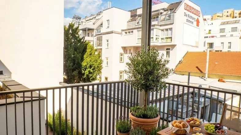 Gemütlicher Balkon mit Holzboden, Frühstückstisch und Blick auf die umliegenden Gebäude.