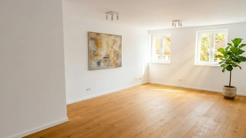 Heller, leerer Raum mit Holzboden, weißen Wänden und zwei Fenstern, ideal als Wohnzimmer.