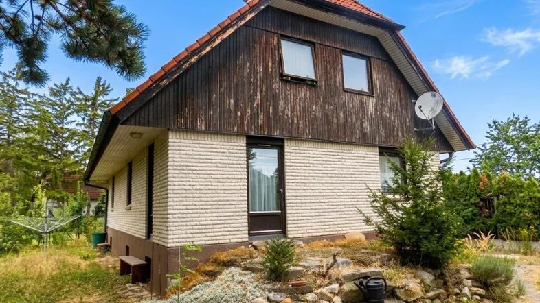 Älteres Einfamilienhaus mit Ziegeldach und verwitterter Holzfassade im oberen Bereich.