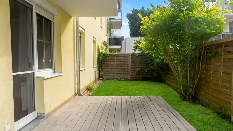 Kleine Holzterrasse mit angrenzendem Rasen und Sichtschutz in einem Neubau.
