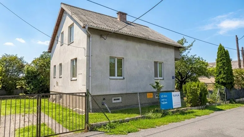 Einfamilienhaus mit Satteldach und Vorgarten in ländlicher Umgebung unter blauem Himmel.