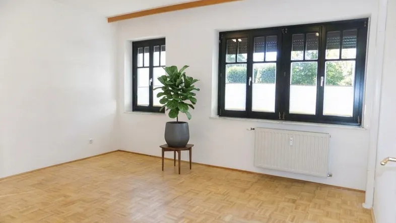 Helles Zimmer mit Parkettboden und großen Fenstern, die viel Tageslicht hereinlassen.