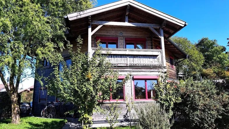 Charmantes Holzhaus mit traditioneller Architektur und rotem Fensterrahmen, umgeben von viel Grün.