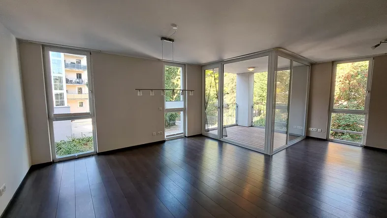Helles Wohnzimmer mit dunklem Holzboden und Zugang zu einem verglasten Balkon.
